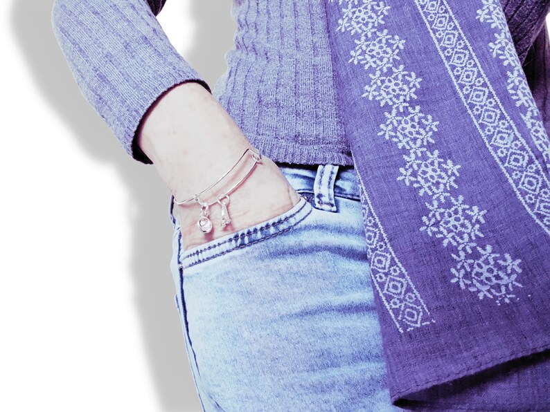 May include: A silver charm bracelet with a bell and a bone charm. The bracelet is worn on a person's wrist, and the person is wearing a gray sweater and blue jeans.