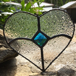 May include: A stained glass heart-shaped window hanging with a turquoise blue diamond in the centre. The glass is textured and clear with black lead lines.