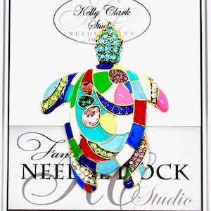 May include: A colorful enamel and rhinestone turtle brooch with a mosaic design. The turtle is on a white card with the text "Kelly Clark Studio Needlepoint".