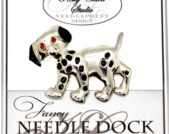 Puede incluir: Broche plateado con forma de perro con manchas y detalles negros. El perro tiene ojos rojos y orejas y nariz negras. El broche está sobre un fondo blanco con el texto "Kelly Clark Studio NEEDLEPOINT DESIGN" y "Fancy NEEDLE DOCK Studio".