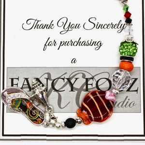 May include: A colorful charm bracelet with a flip-flop charm, a seashell charm, a fish charm, and various beads. The bracelet is on a white card with the text "Thank You Sincerely for purchasing a FANCY FOZ Studio".