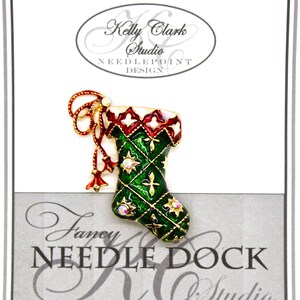 May include: A green and red Christmas stocking pin with gold trim and rhinestones. The pin is on a white card with the text "Kelly Clark Studio Needlepoint Design" and "Fancy Needle Dock KC Studio".