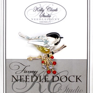 Puede incluir: Broche con forma de pájaro con cabeza negra, alas plateadas y pecho amarillo, posado en una rama dorada con bayas rojas y cristales transparentes. La broche está sobre un fondo blanco con el texto "Kelly Clark Studio NEEDLEPOINT DESIGN" y "Fancy NEEDLE DOCK Studio".