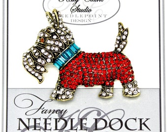 Puede incluir: Un broche rojo y dorado con forma de perro terrier escocés adornado con joyas. El perro lleva un collar de color azul turquesa adornado con joyas. El broche está sobre un fondo blanco con el texto "Kelly Clark Studio Needlepoint Design" y "Fancy Needle Dock Studio".