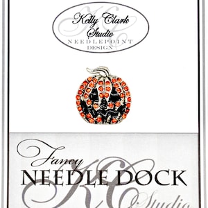 Puede incluir: Un broche de calabaza plateado con detalles en naranja y negro. La calabaza está adornada con pedrería naranja y tiene una cara tallada. El broche está sobre un fondo blanco con el texto "Kelly Clark Studio NEEDLEPOINT DESIGN" y "Fancy NEEDLE DOCK Studio".
