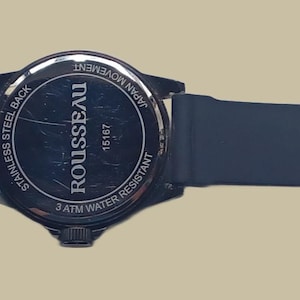 K&ouml;nnte beinhalten: Eine schwarze Armbanduhr mit Silikonarmband und Dornschlie&szlig;e. Der runde Geh&auml;useboden besteht aus Edelstahl und tr&auml;gt den in Wei&szlig; auf die dunkle Oberfl&auml;che gedruckten Text ROUSSEAU, 5 ATM WATER RESISTANT und JAPAN MOVEMENT.