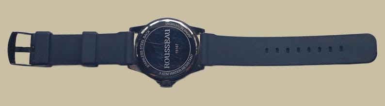 K&ouml;nnte beinhalten: Eine schwarze Armbanduhr mit Silikonarmband und Dornschlie&szlig;e. Der runde Geh&auml;useboden besteht aus Edelstahl und tr&auml;gt den in Wei&szlig; auf die dunkle Oberfl&auml;che gedruckten Text ROUSSEAU, 5 ATM WATER RESISTANT und JAPAN MOVEMENT.