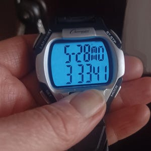 May include: A Champion digital watch with a black strap and silver bezel. The watch face displays the time as 5:28 and a four-digit number. The watch has buttons labeled LAP RESET, ST.STP, SET, and MODE.