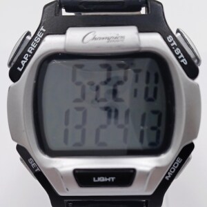 May include: A digital Champion watch with a silver face and black accents. The watch displays the time and date. It has buttons labeled LAP.RESET, ST.STP, SET, MODE, and LIGHT. The Champion logo is visible on the watch face.