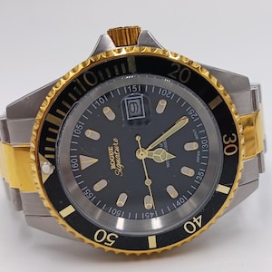 May include: A two-tone wristwatch with a black dial and gold accents. The watch features a gold bezel with black markings, a date window, and the text "ROGUE Signature". The watch band is silver and gold.
