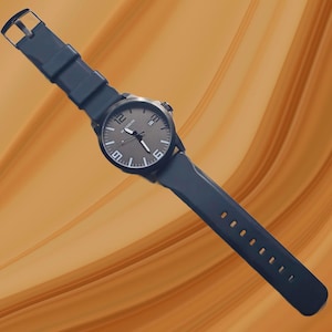 K&ouml;nnte beinhalten: Eine Armbanduhr mit dunkelgrauem, kreisf&ouml;rmigem Zifferblatt, wei&szlig;en arabischen Ziffern auf den 12-, 6- und 9-Uhr-Positionen, wei&szlig;en Stundenmarkierungen und einem Datumsfenster auf 3 Uhr. Die Uhr hat ein dunkelblaues Silikonarmband mit Metallschnalle.