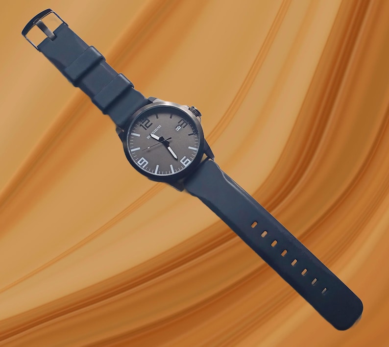 K&ouml;nnte beinhalten: Eine Armbanduhr mit dunkelgrauem, kreisf&ouml;rmigem Zifferblatt, wei&szlig;en arabischen Ziffern auf den 12-, 6- und 9-Uhr-Positionen, wei&szlig;en Stundenmarkierungen und einem Datumsfenster auf 3 Uhr. Die Uhr hat ein dunkelblaues Silikonarmband mit Metallschnalle.