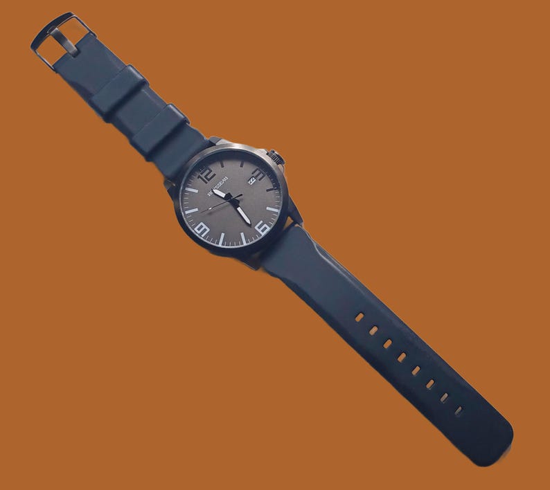 K&ouml;nnte beinhalten: Eine dunkelblaue Armbanduhr mit rundem Geh&auml;use, dunkelgrauem Zifferblatt, wei&szlig;en Stundenmarkierungen und gro&szlig;en wei&szlig;en Ziffern auf den 12-, 6- und 9-Uhr-Positionen. Die Uhr verf&uuml;gt &uuml;ber ein Datumsfenster und ein flexibles dunkelblaues Silikonarmband.