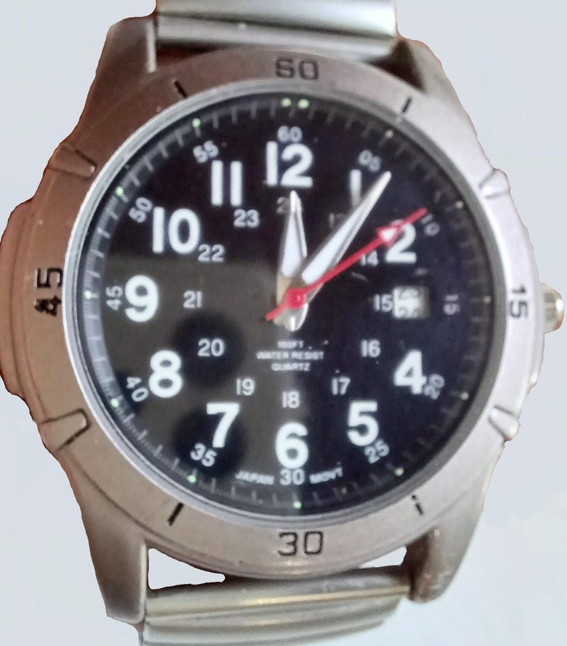 K&ouml;nnte beinhalten: Eine silberfarbene Armbanduhr mit schwarzem Zifferblatt. Die Uhr hat wei&szlig;e Ziffern, wei&szlig;e Zeiger und einen roten Sekundenzeiger. Auf dem Zifferblatt steht "100FT WATER RESIST QUARTZ" und "JAPAN 30 MOVT".