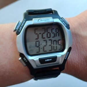 May include: A Champion digital watch with a silver face and black accents. The watch displays the time and has buttons labeled "LAR RESET", "BT.STP", "SET", "MODE", and "LIGHT". The watch is on a wrist.