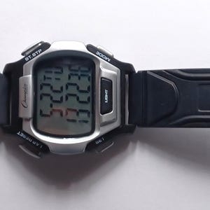 May include: A digital wristwatch with a black rubber strap and a silver-colored face. The watch displays the time and date on a digital screen. The strap has a buckle closure and multiple adjustment holes. The watch is designed for everyday wear.