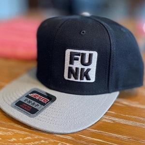 Könnte beinhalten: Schwarze und graue Baseballkappe mit einem weißen Patch, auf dem "FU NK" in schwarzen Buchstaben steht.