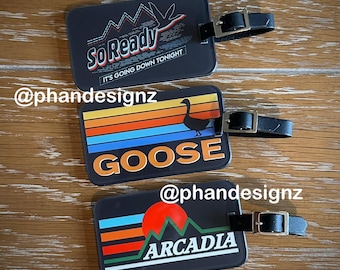 May include: Three black luggage tags with colorful retro designs. The top tag says "So Ready It's Going Down Tonight". The middle tag says "Goose" with a silhouette of a goose. The bottom tag says "Arcadia" with a mountain silhouette.