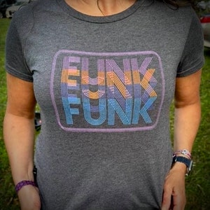 Könnte beinhalten: Ein heidefarbenes T-Shirt mit einer Retro-Grafik des Wortes "FUNK", das dreimal in einem Kasten wiederholt wird. Die Grafik ist in Blautönen, Orange und Lila gehalten.