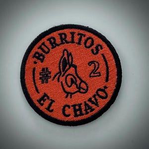 Op de afbeelding: Een ronde, geborduurde patch met een rode achtergrond en zwarte rand. De patch toont de tekst "BURRITOS 2 EL CHAVO" in een cirkelvormig patroon, samen met een gestileerde ezelillustratie.