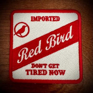 Könnte beinhalten: Red Bird Marken-Patch mit einem roten Vogel-Logo und dem Text "IMPORTED Red Bird DON'T GET TIRED NOW" in Weiß.
