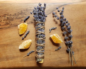 May include: A bundle of dried lavender tied with twine, surrounded by small pieces of orange calcite crystals on a wooden surface.