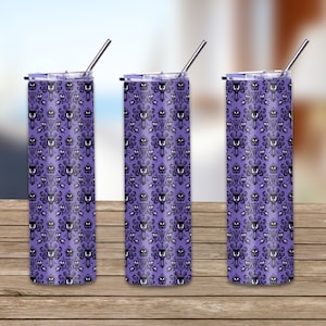 May include: Three stainless steel tumblers with a purple background and a repeating black pattern of spooky mansion faces. Each tumbler has a silver straw and a matching lid. The tumblers are on a wooden surface.