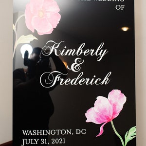 May include: Black wedding welcome sign with white text and pink floral accents. The sign reads "Welcome to the Wedding of Kimberly & Frederick" and includes the date and location: Washington, DC, July 31, 2021.