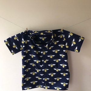 May include: A navy blue short-sleeved button-up shirt with a repeating pattern of yellow and white bees.