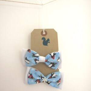 May include: Two blue bow ties with white trim and a penguin pattern. The bow ties are hanging from a brown tag with a squirrel silhouette.