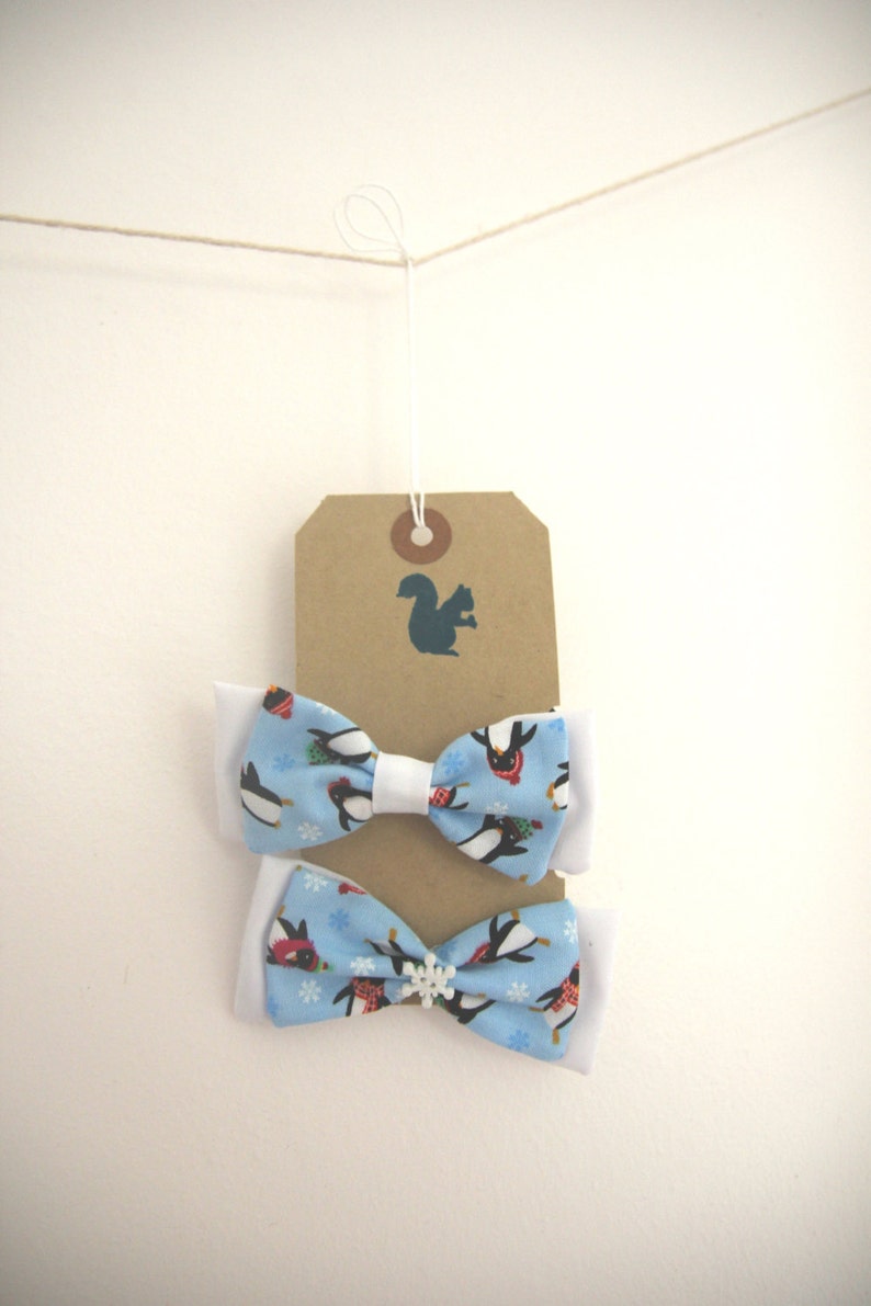 May include: Two blue bow ties with white trim and a penguin pattern. The bow ties are hanging from a brown tag with a squirrel silhouette.