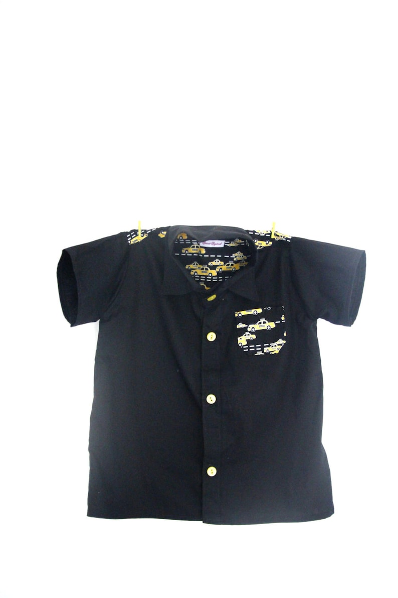 Puede incluir: Camisa negra de manga corta con botones y estampado de taxi amarillo en el interior del cuello y el bolsillo.
