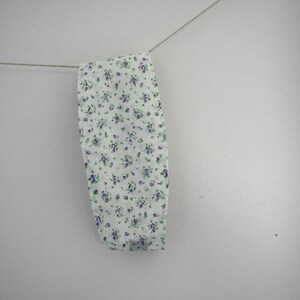May include: A white fabric headband with a small purple and green floral pattern.