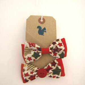 May include: Two red and white bow ties with a gold star pattern and a red button. The bow ties are hanging from a brown tag with a squirrel silhouette.