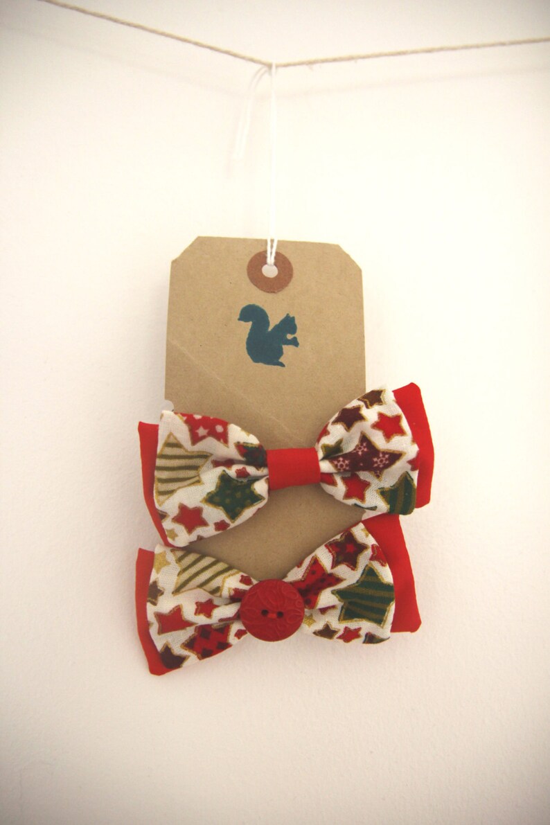 May include: Two red and white bow ties with a gold star pattern and a red button. The bow ties are hanging from a brown tag with a squirrel silhouette.