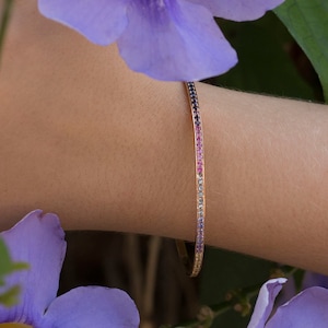 May include: A delicate gold bangle bracelet with a rainbow of tiny gemstones set in a continuous line.