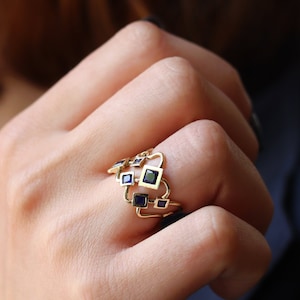 May include: A gold ring with a geometric design featuring multiple square-shaped blue gemstones.