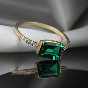 May include: A gold ring with a large emerald green gemstone and a row of small diamonds set in the band.
