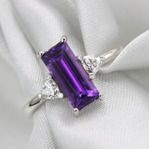 May include: A silver ring with a purple rectangular gemstone and two smaller triangular gemstones on either side