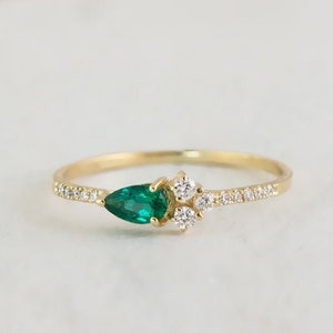 May include: A delicate gold ring with a pear-shaped emerald gemstone and smaller round diamonds set in a pave band.