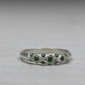 Puede incluir: Un anillo de banda de plata con un dise&ntilde;o delicado que presenta una fila de peque&ntilde;as piedras preciosas verdes.