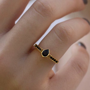 May include: A gold ring with a teardrop-shaped black gemstone and a band of smaller black gemstones.