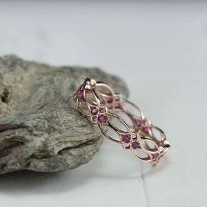 May include: A delicate rose gold band ring with a delicate, intricate design featuring a series of small pink gemstones.