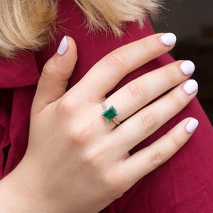 May include: A gold ring with a square emerald green gemstone surrounded by smaller diamonds.
