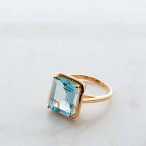 May include: A gold ring with a large, square-shaped, light blue gemstone.