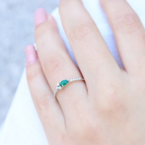 May include: A delicate silver ring with a pear-shaped green gemstone and small white gemstones set in a band of tiny white gemstones.