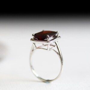 Puede incluir: Un anillo de plata con una gran piedra preciosa de color rojo oscuro engastada en un bisel cuadrado.
