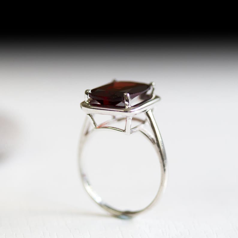 Puede incluir: Un anillo de plata con una gran piedra preciosa de color rojo oscuro engastada en un bisel cuadrado.
