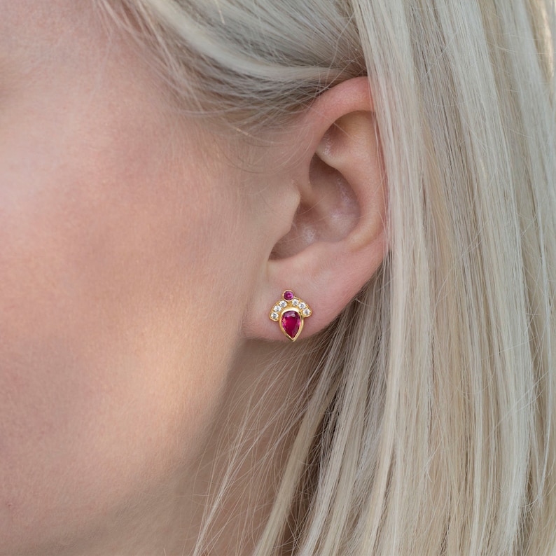 Pode incluir: Um par de brincos de ouro com uma gema de rubi em forma de l&aacute;grima e um halo de gemas brancas menores.