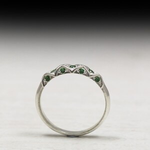 Puede incluir: Un anillo de banda de plata con una fila de peque&ntilde;as piedras preciosas verdes engastadas en un dise&ntilde;o delicado.